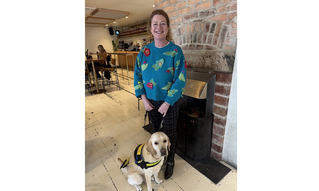 Angela stands in front of a fire place with Yuki, a yellow labrador Seeing Eye Dog