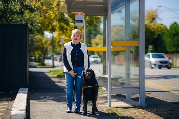 A woman stands on a footpath next to her black labrador Seeing Eye Dog