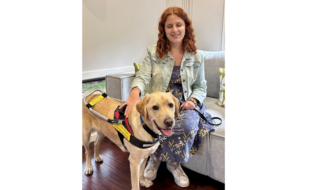 Lilly sits on a lounge with Teddy, a yellow labrador, standing in front of her.