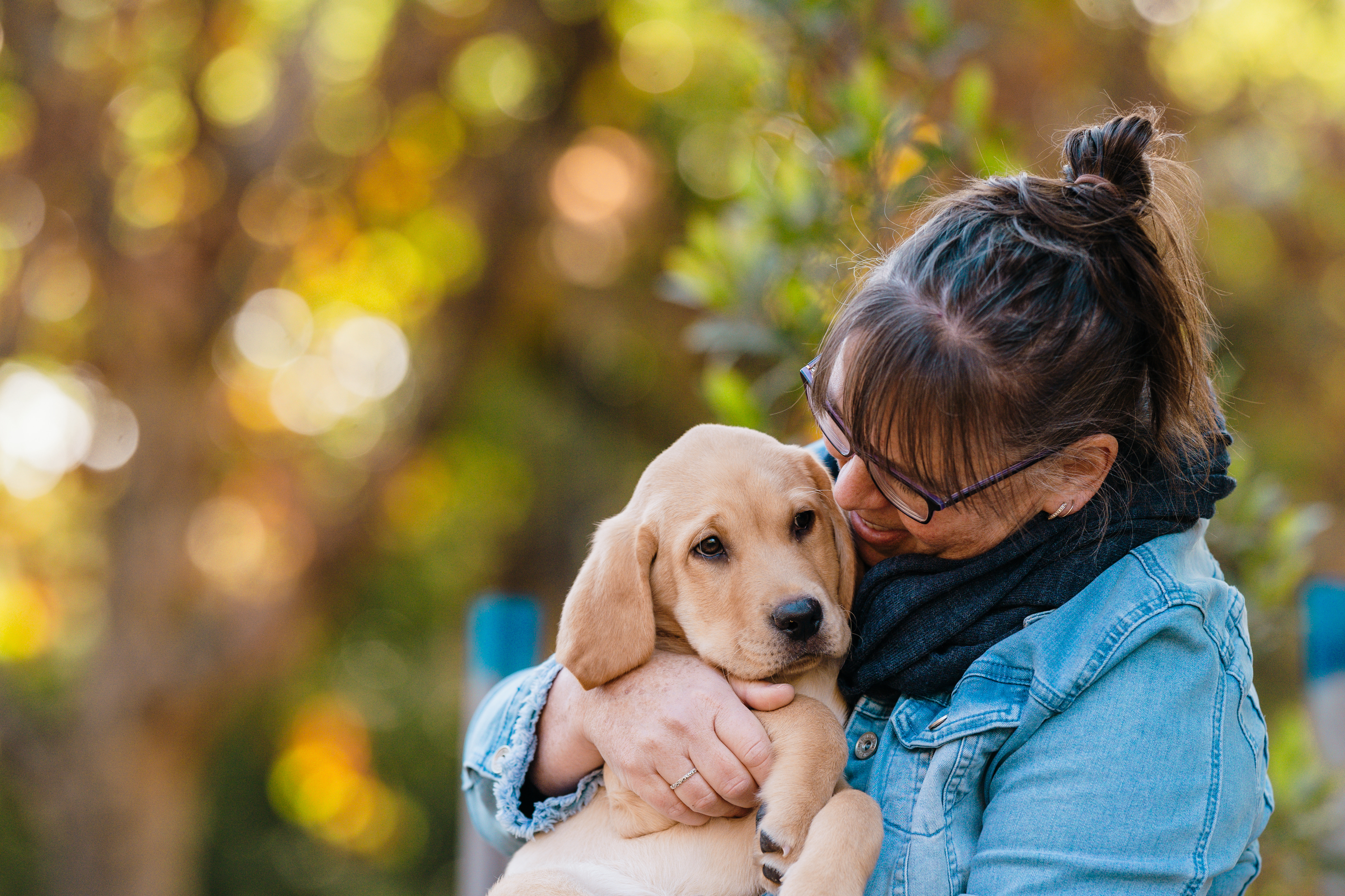 Narelle hugs a small yellow Seeing Eye Dogs puppy, with trees behind them. 