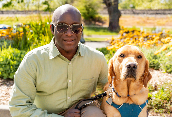 Nemoy, wearing sunglasses and sitting outdoors, next to his Seeing Eye Dog, Benji.