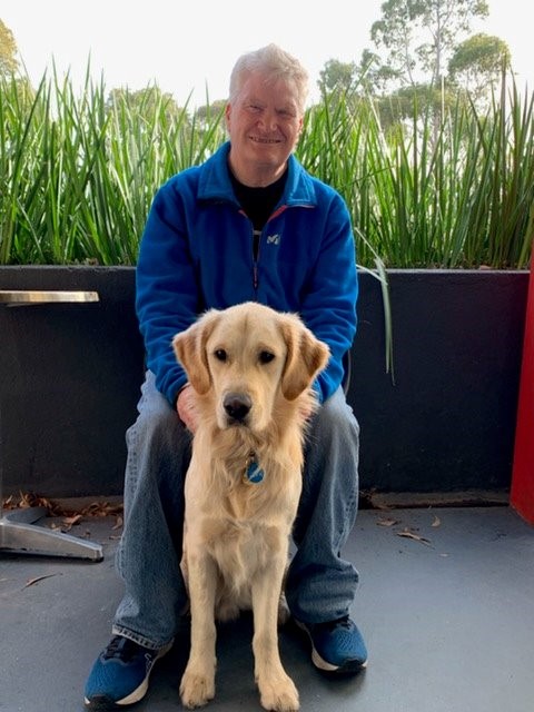 Nick is standing outside, behind his Seeing Eye Dog.