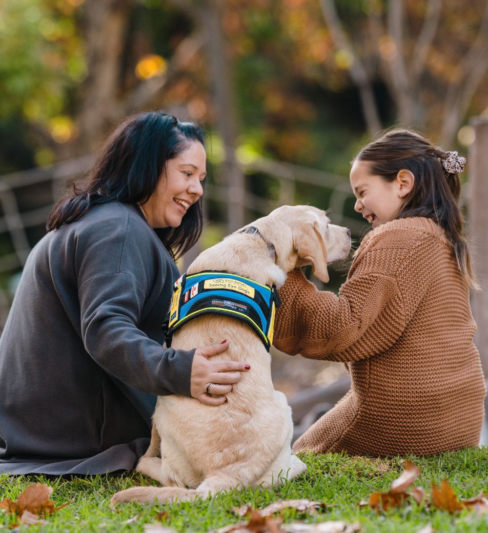 A woman and a girl are sitting on either side of a yellow Seeing Eye Dog;