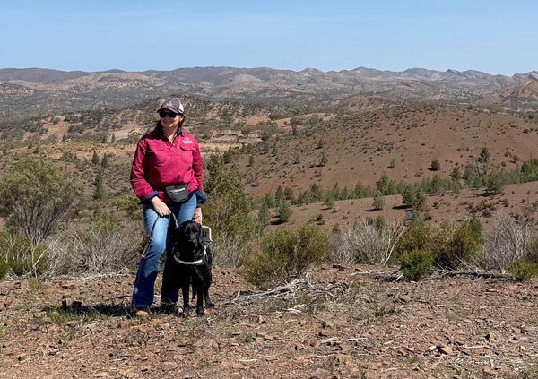 Tarina and Mika, a black labrador, stand together on a hill at a sheep station.