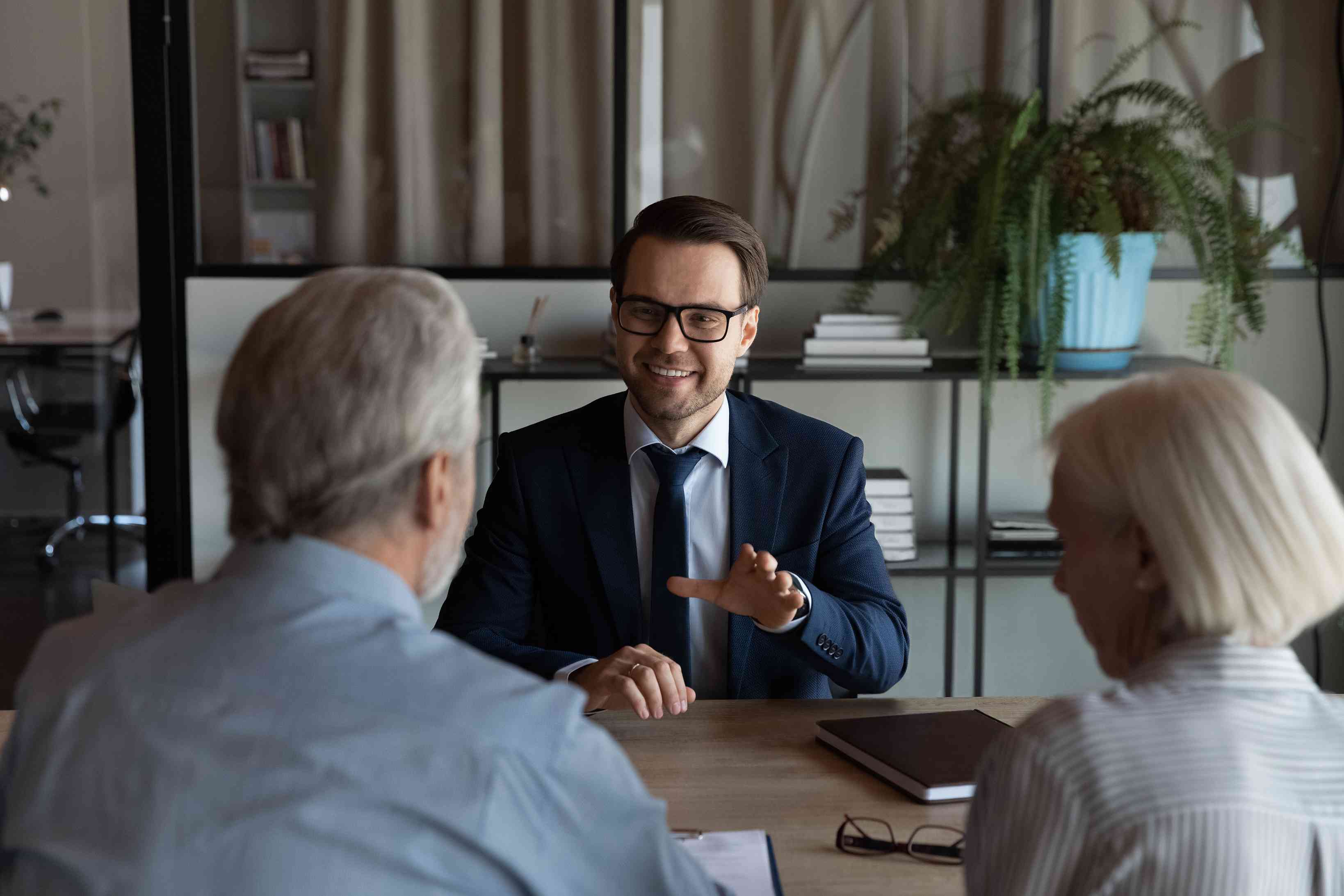 A man and a woman are sitting across the desk from a male solicitor. He is wearing glasses and smiling,