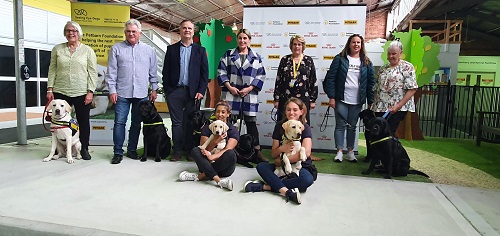 A group of Seeing Eye Dog handlers stand with their Seeing Eye Dogs, while two staff sit with puppies