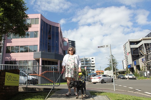 A woman stands on a footpath with a black Seeing Eye Dog