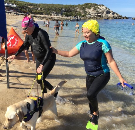 At the beach, Monika and a sighted guide along with Junior are exiting the water after swimming