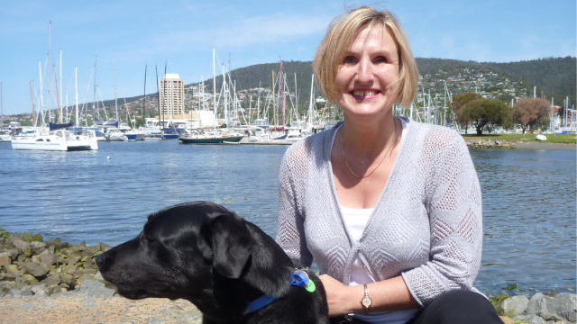 Jen and her Seeing Eye Dog pictured by a waterfront with boats in the background