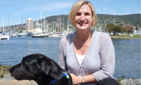 Jen and her Seeing Eye Dog pictured by a waterfront with boats in the background