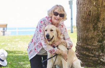 Therese is kneeling and embracing Yael, a Golden Retriever Seeing Eye Dog