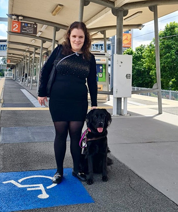 Isabella is smiling at the camera while holding the harness of her black labrador Seeing Eye Dog, Penny