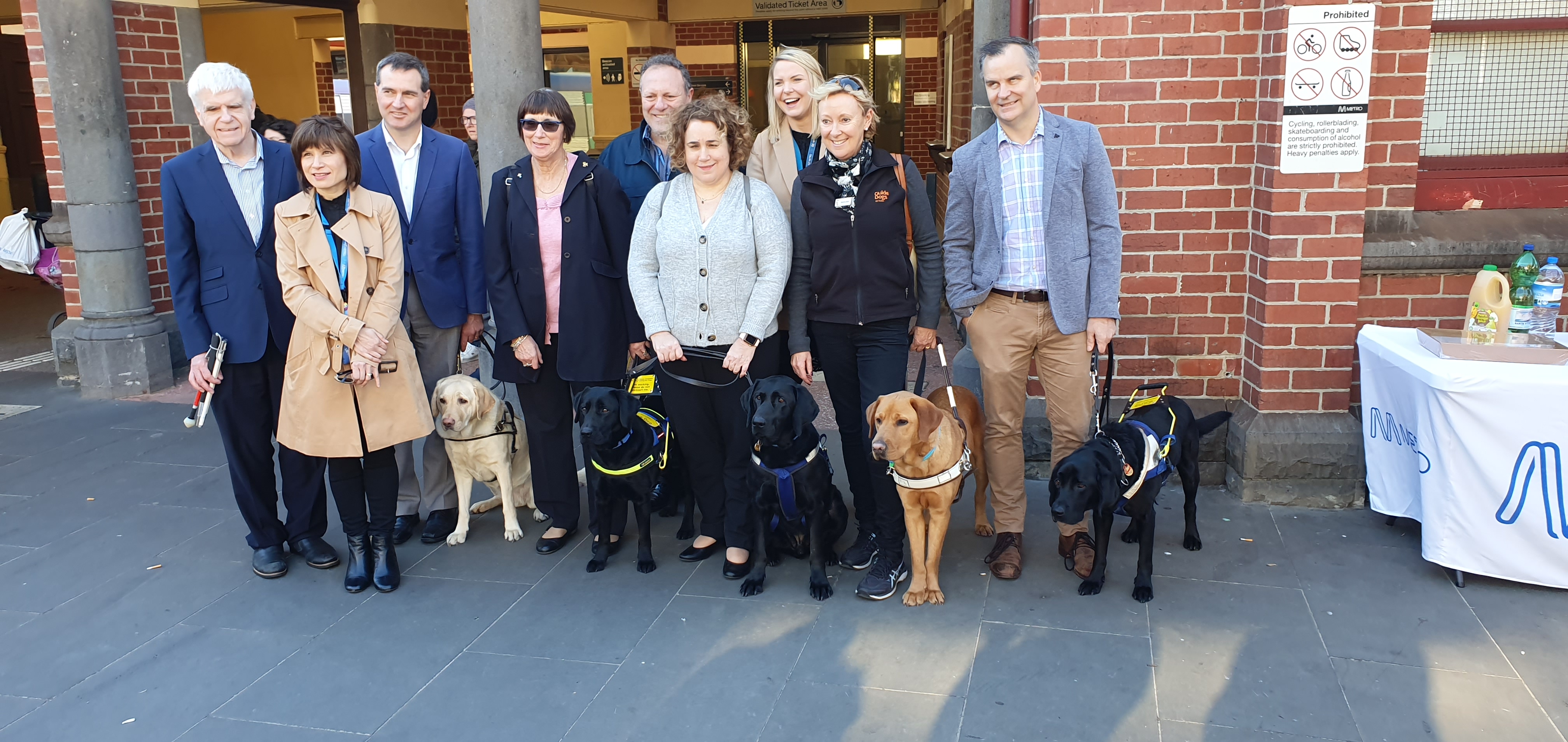 Metro Trains staff and clients from Vision Australia Seeing EYE Dogs and Guide Dogs Victoria stand at Footscray Station with their assistance dogs.