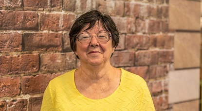 Anne in front of a brick wall wearing a yellow top